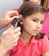 A doctor examining the inside of a young girl's ear while her mother looks on.