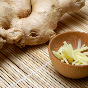 Whole ginger root and chopped up ginger on a bamboo table mat.