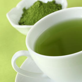 A bowl of fresh green tea leaves and a cup of brewed green tea. 